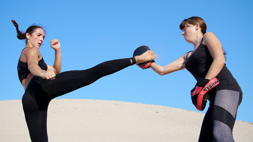 Two athletic, young women in black fitness suits are engaged in a pair work out kicks train to fight