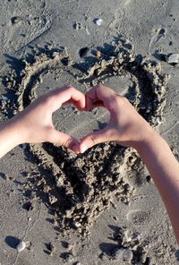 Cropped image of person making heart shape with hand on shore