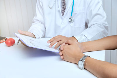 Midsection of doctor explaining medical records to patient