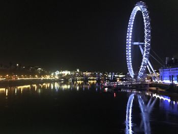 Illuminated city by river against sky at night