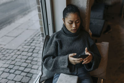 Young businesswoman using mobile phone by window at office