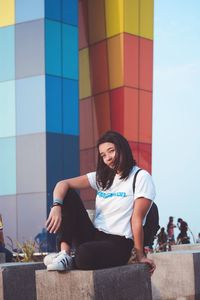 Portrait of smiling young woman sitting against wall