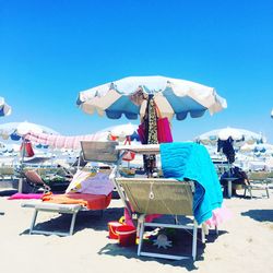 Lounge chairs by parasols at beach against clear blue sky