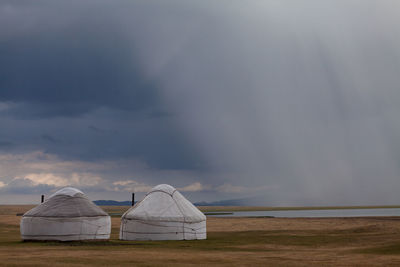 Yurts by song kol lake against cloudy sky