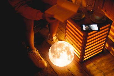 Low section of person reading book with illuminated sphere