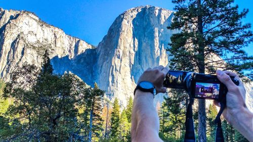 Man photographing through smart phone against clear sky