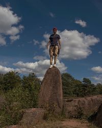 Rear view of boy standing on rock against sky
