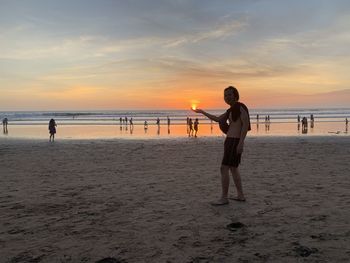 People standing on beach against sky during sunset