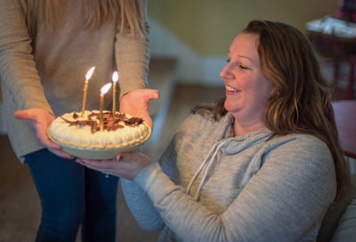 Midsection of woman giving lit birthday cake to friend at home