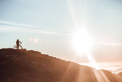 Side view of guy in helmet riding on bicycle on top of mountain with beautiful sunset