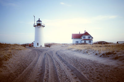 Lighthouse by road amidst buildings against sky