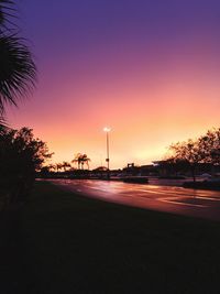 Road by trees against sky during sunset