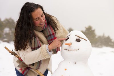 Woman making snowman during winter against sky
