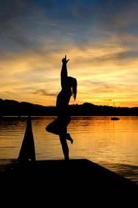 Silhouette woman doing yoga by lake against sky