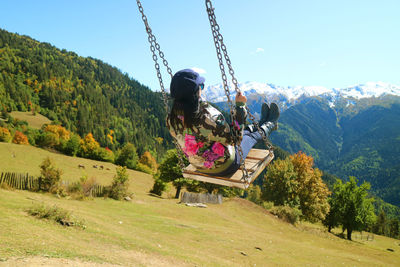 Woman sitting on swing against mountains and sky