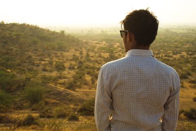 Rear view of young man standing on mountain against sky