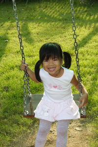 Portrait of smiling girl sitting on swing at playground