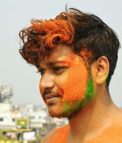Close-up of man with orange powder paint on face against sky