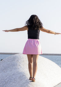 Rear view of woman with arms raised against sea