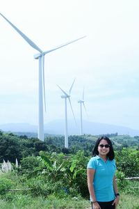 Portrait of smiling woman standing on land against windmills and sky