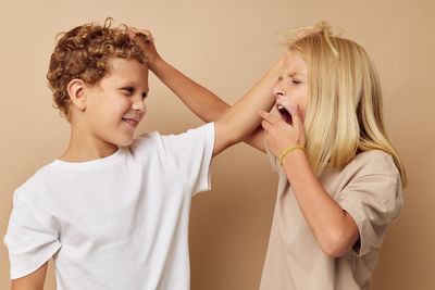 Portrait of sibling fighting against beige background