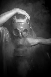 Man in raincoat wearing gas mask against black background