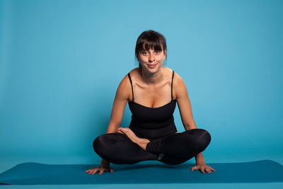 Portrait of smiling woman exercising against blue background
