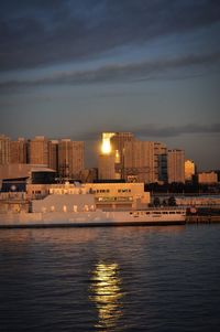 Sea by illuminated city against sky at sunset