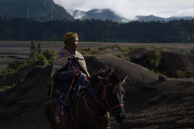 Man looking away while riding horse against landscape 