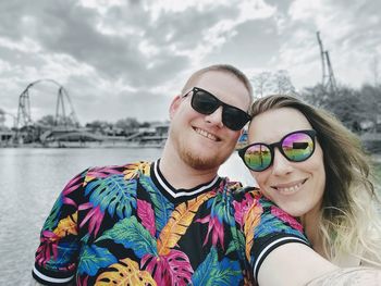 Portrait of smiling woman wearing sunglasses while standing against lake