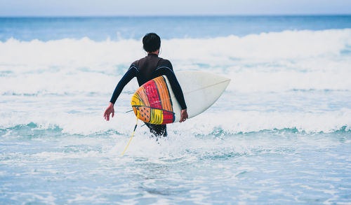 Rear view of man holding surfboard in sea