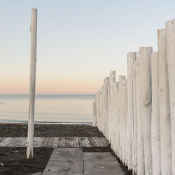 Wooden posts on beach against sky during sunset