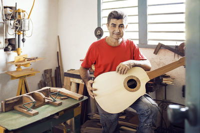 Portrait of man holding guitar while standing in workshop