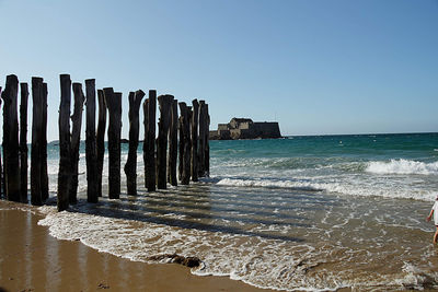 Wooden posts on beach against clear sky