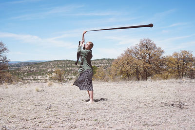 Side view of young woman spinning textile while standing on land against sky during sunny day
