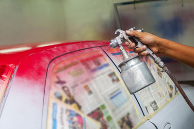 Cropped worker hand painting red on car at garage