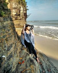 Young woman standing on cliff by sea against sky