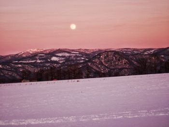 Snow covered land and mountains against sky during sunset