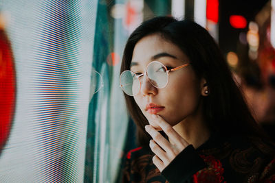 Portrait of young woman standing against illuminated city at night