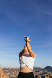 Slim unrecognizable female in casual outfit performing mountain with arms up and backbend posture on slope of rocky mountain