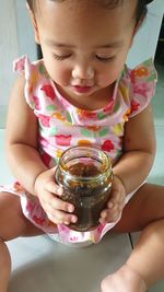 Close-up of cute baby girl holding container while sitting at home