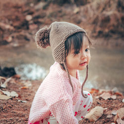 Cute baby girl looking away while crouching on land during winter