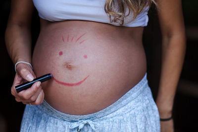 Midsection of pregnant woman drawing on stomach against black background