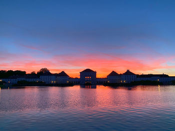 Lake by buildings against sky during sunset