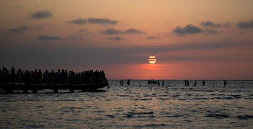 Silhouette people on beach against sky during sunset