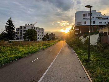 Road by buildings against sky during sunset in city