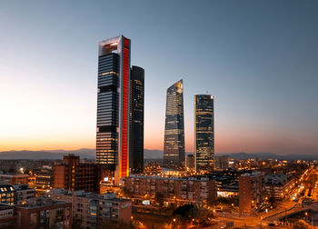 Illuminated buildings in city against clear sky during sunset