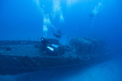 High angle view of scuba divers swimming over ship wreck undersea