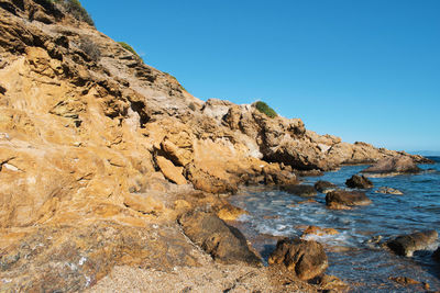 Rock formation in sea against clear blue sky