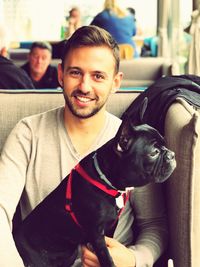 Portrait of handsome young man with dog sitting on sofa